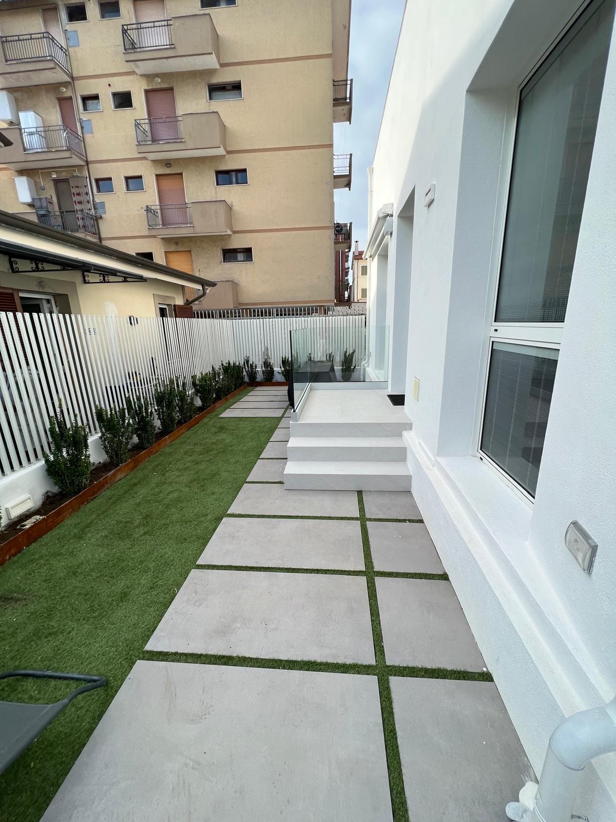 Il camminamento laterale di FRAME: lastre di gres posate a giunto erboso e la siepe lungo la recinzione.
