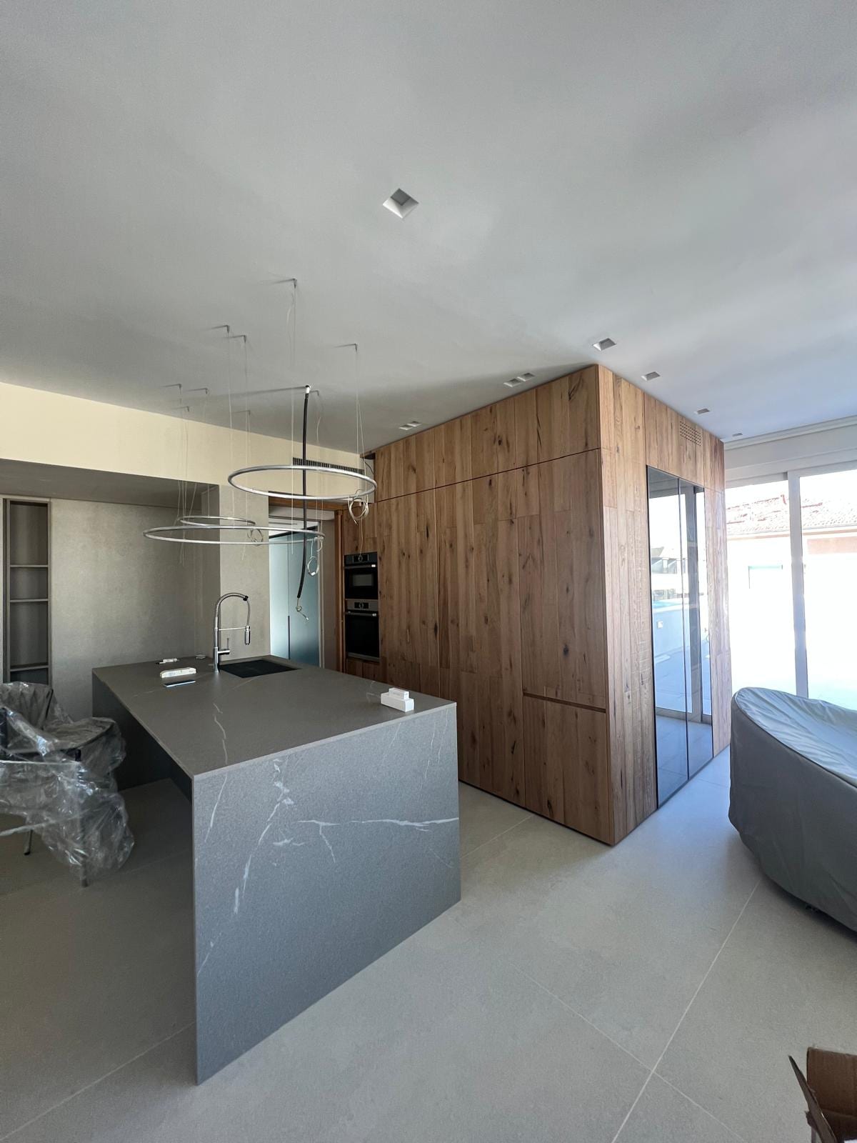 Cucina di FRAME: isola in pietra grigia davanti al volume rivestito in rovere che contiene i vani tecnici.