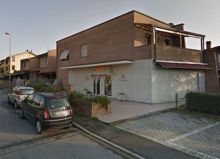Il fondo commerciale di Unità Fermi al piano terra dell’edificio d’angolo, con la loggia in laterizio sopra.