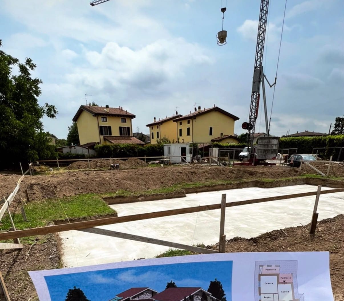 Cantiere all’avvio: la platea di fondazione appena gettata nello scavo, la gru con la benna del calcestruzzo e, in primo piano, la tavola di progetto.