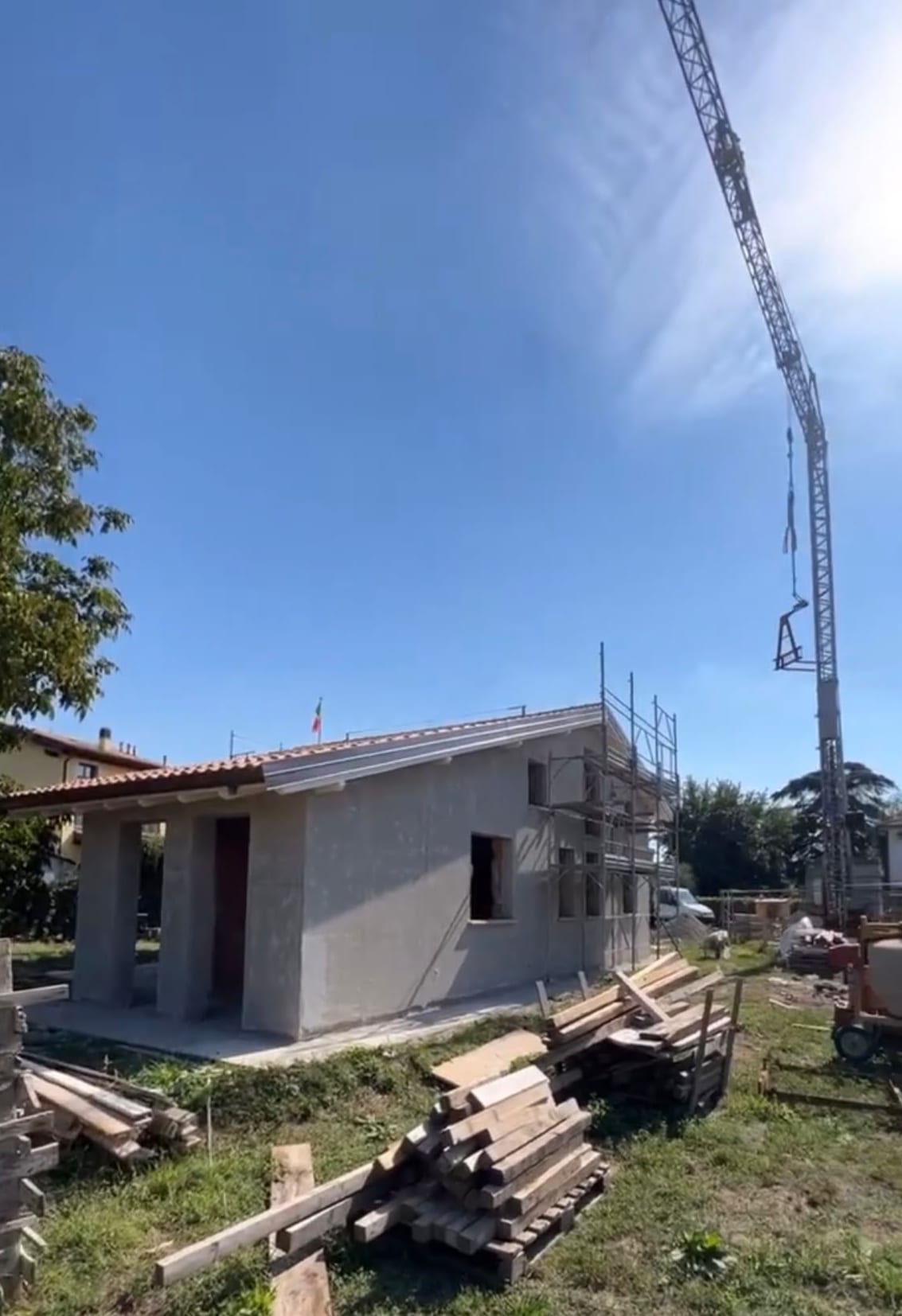 Edificio al grezzo: le murature intonacate a rustico, la copertura in coppi già posata, il ponteggio sul fianco e la gru a torre contro il cielo.